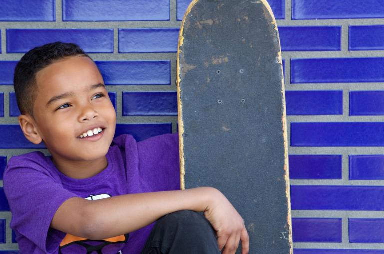 Close up portrait of a cute kid smiling outdoors with skateboard