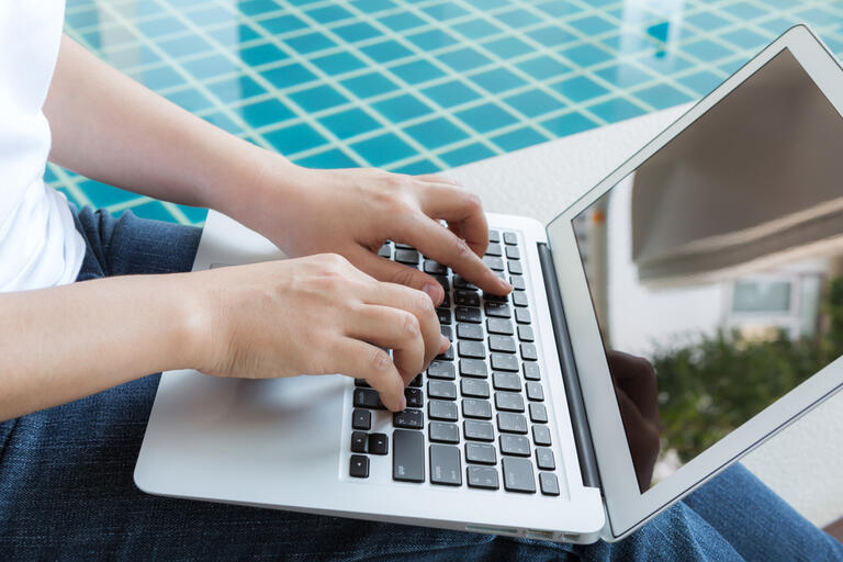 Woman working with laptop computer sitting at swimming pool