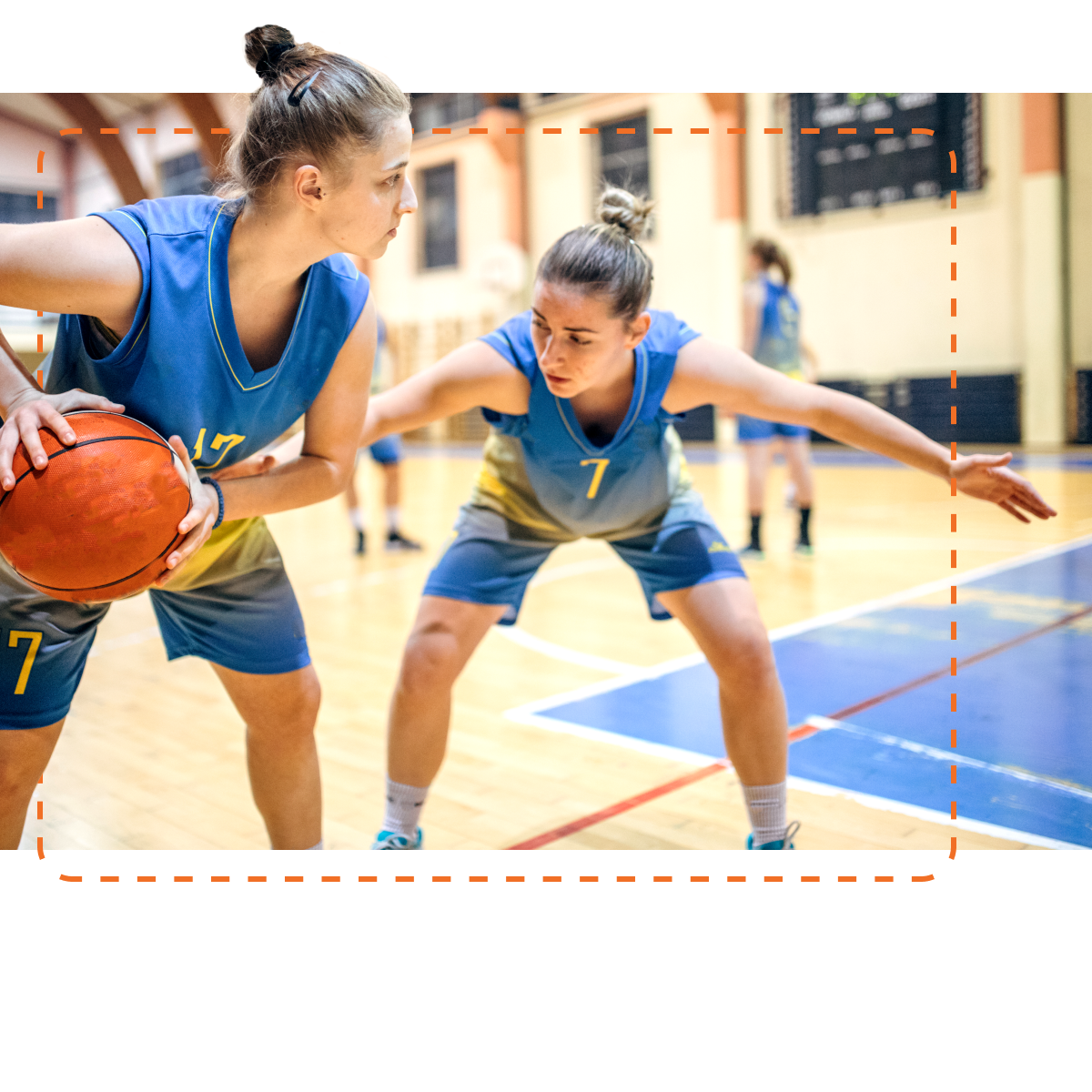 Two female basketball players in blue and gold uniforms practice on the court, with one player holding the ball in preparation to make a move while the other defends, demonstrating teamwork and focus during a training session.